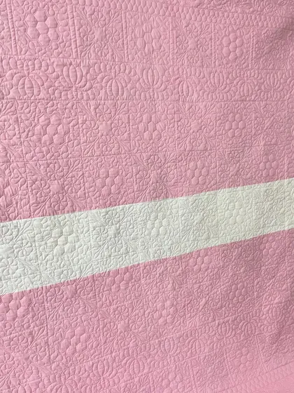 A close-up of the intricate quilting on the back of the pink hexagon quilt.