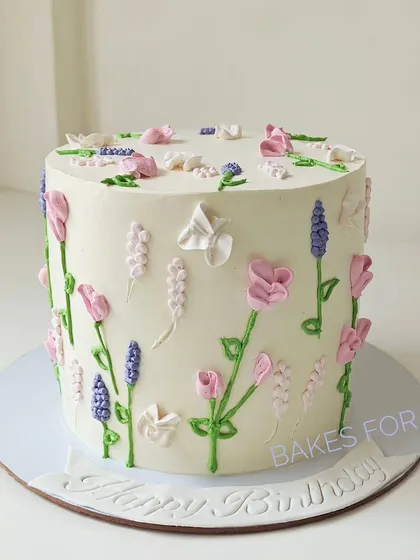 A clean and simple white cake decorated with hand-piped wildflowers in shades of pink and lavender. This design is a testament to the beauty of minimalist buttercream art.