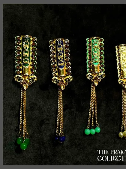 Our collection of long, dangling brooches with colored beads. These pieces feature detailed enamel work on a gold-tone base and are finished with hanging chains and beads in green and blue.