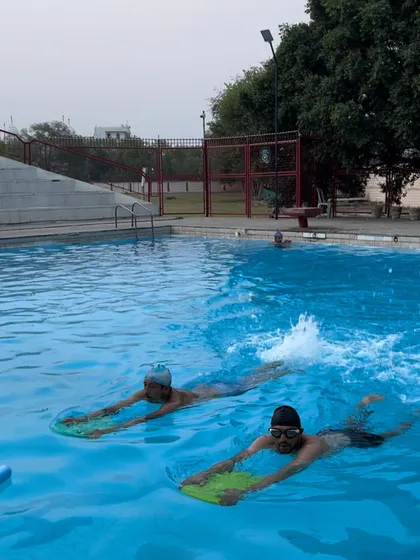 Two adult learners practice their kicking technique using kickboards in the main pool area. This exercise is crucial for developing leg strength and getting comfortable with moving through the water.