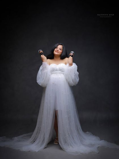 A playful and happy portrait, with the mother-to-be joyfully holding up baby shoes. Her expression is one of pure excitement.