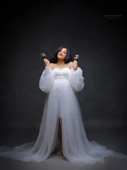 A playful and happy portrait, with the mother-to-be joyfully holding up baby shoes. Her expression is one of pure excitement.