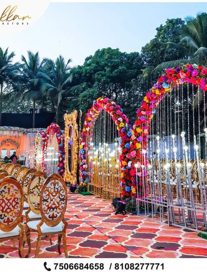 A vibrant and colorful entrance for an outdoor wedding. The aisle is lined with floral arches in a rainbow of colors, creating a joyful and celebratory pathway for guests.