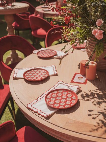 The tables are set with custom-printed plates and scalloped napkins, ensuring every detail aligns with the 'Gulal Bagh' theme.