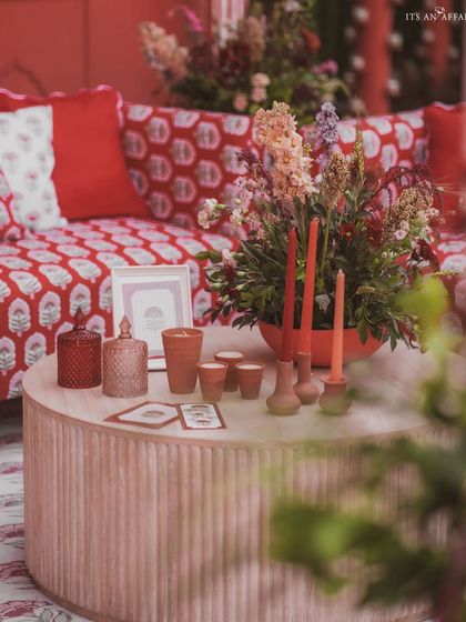 A close-up of a coffee table, styled with custom-printed cushions, colorful florals, and unique candle holders.