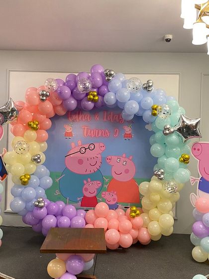 A fun Peppa Pig theme for a twins' birthday party. This setup features a full circular balloon arch in rainbow pastels and cutouts of Peppa and George Pig.