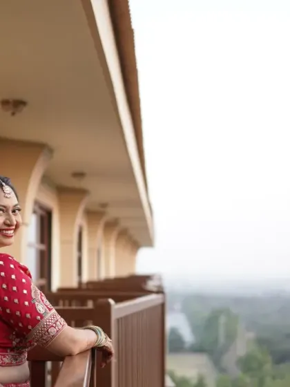 A beautiful bride enjoying the view before her ceremony. The natural light highlights her glowing skin and the intricate details of her red and teal Gujarati lehenga.