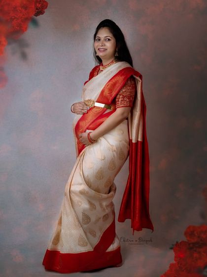 A beautiful profile shot of a mom-to-be in a classic cream and red saree. The soft lighting creates a gentle and timeless feel.