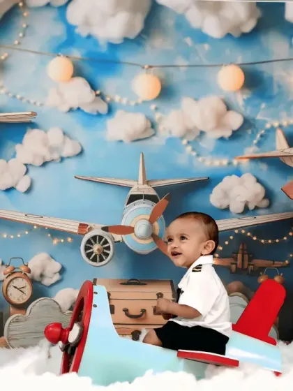 This little pilot looks to the side with a curious expression, sitting in his plane amidst a backdrop of clouds and vintage airplanes.