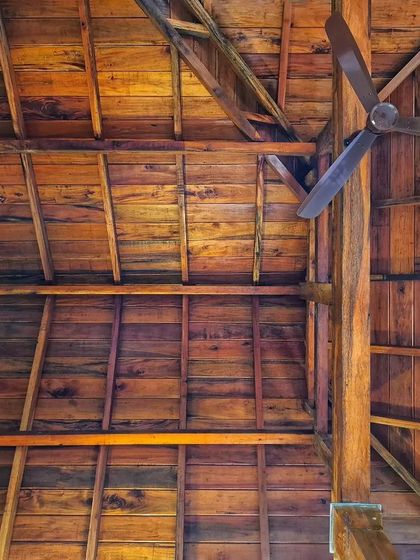 A worm's-eye view of the wooden truss work for a sloping roof. The complex joinery and the rich grain of the reclaimed wood are on full display, showcasing the structural and aesthetic elegance of timber construction.
