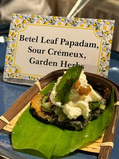 A creative appetizer featuring Betel Leaf Papadam with Sour Crémeux and Garden Herbs. This dish combines the pungent flavour of betel leaf with a creamy, tangy topping for a complex and refreshing bite.