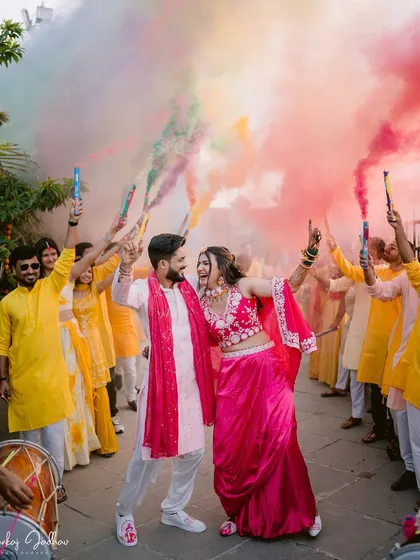A vibrant explosion of color and joy! This shot from a Haldi ceremony, with friends and family surrounding the couple with color smoke, captures the high-energy, fun-filled moments that precede the wedding.