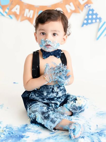 A classic blue-themed cake smash, where this little boy is covered head to toe in blue frosting, making for a memorable first birthday photo.