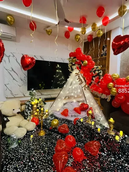 A cozy and romantic floor seating arrangement. I created a small tent with a sequined blanket, a canopy of lights, and surrounded it with balloons, candles, and a teddy bear for a perfect date night at home.