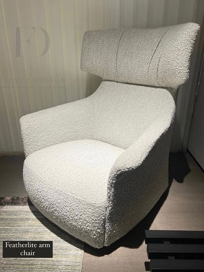 The 'Featherlite' armchair, upholstered in a white, highly-textured bouclé fabric. Its high, winged headrest provides a sense of privacy and comfort, creating a cozy personal retreat.