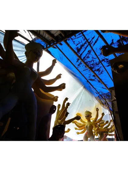 Unfinished idols of the goddess Durga are seen through a blue tarp at a workshop ahead of the Durga Puja festival. The light filtering through creates dramatic silhouettes of the multi-armed figures.
