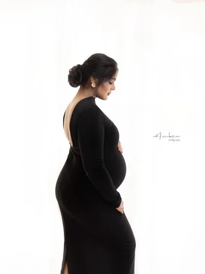 The elegance of a backless black gown is showcased in this side profile portrait. The clean white background puts all the focus on her form, creating a sophisticated and modern maternity photograph.