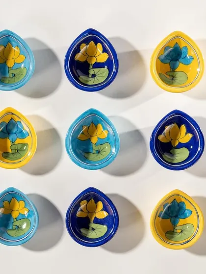 A minimalist flat lay of hand-painted ceramic diyas from Doro. The clean, geometric arrangement on a white background highlights the vibrant colors and artistic detail of each piece.