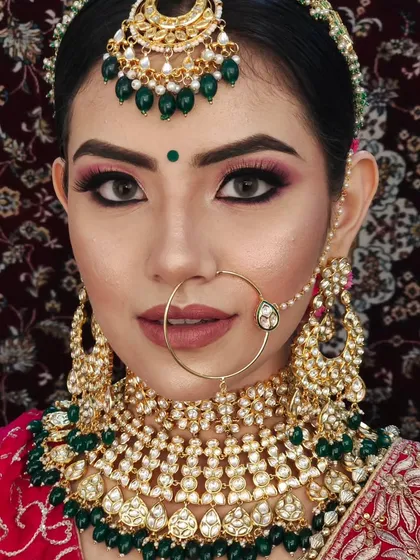 A close-up of a bride wearing a heavy Kundan choker with green beads. The intricate design of the necklace and nath is clearly visible.