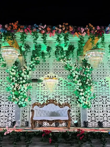 A full view of the green and white themed wedding stage. The symmetrical design with a central sofa, flanked by floral pillars and chandeliers, provides a balanced and picturesque setting.