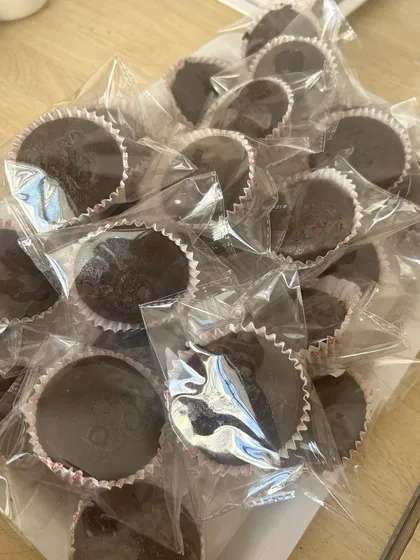 A tray of freshly baked and individually wrapped chocolate cupcakes, a simple yet effective dessert option for large corporate or school gatherings.