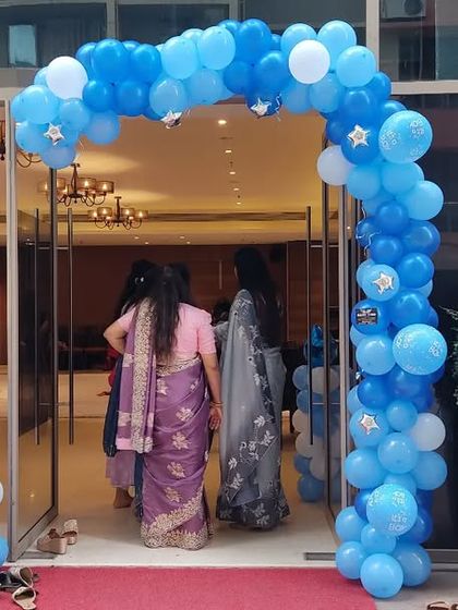 The entrance to a baby welcome party, with a blue balloon arch and baby boy foil balloon pillars.