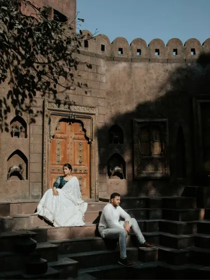 A wide-angle shot capturing the scale of the heritage location. The composition places the couple within the grand architectural setting, telling a story of timeless romance.