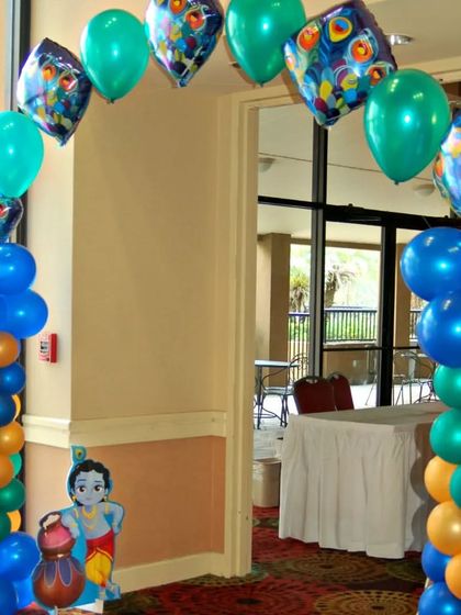 I can create themed balloon arches for any festival. This entrance decoration for a Krishna-themed party uses blue, green, and orange balloons, along with special foil balloons printed with peacock feathers and a cutout of little Krishna.