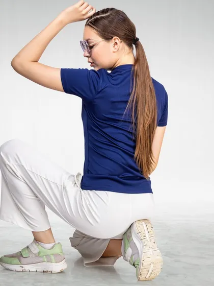 A model in a blue t-shirt and white pants squats in a studio setting. The clean background and dynamic pose are perfect for e-commerce sites that need to show apparel in motion.