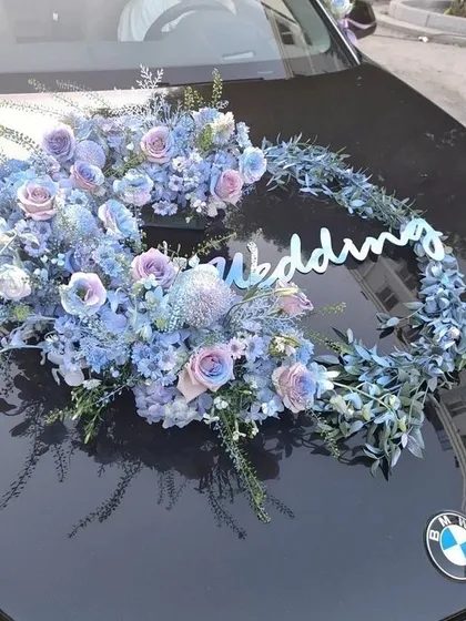 A crescent-shaped fresh flower arrangement for a BMW wedding car. The cool tones of the blue and purple flowers create a sophisticated and modern look.