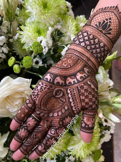 A single hand adorned with a variety of traditional motifs, including elephants, peacocks, and lotuses, beautifully arranged against a floral backdrop.