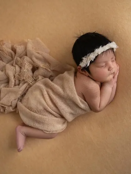 An overhead shot of a newborn in a side pose, with a neutral beige wrap draped beautifully on a matching backdrop.