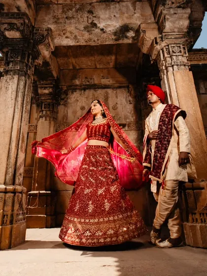 A beautiful portrait of the couple standing together, with the bride's dupatta creating a graceful frame. The warm sunlight and stone background give this shot a timeless, classic feel.