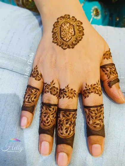 A unique and minimal design for a bride-to-be. It features a small, intricate crest on the back of the hand with detailed floral bands on the fingers.