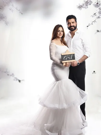 A lovely gender reveal photo. The couple stands together in a dreamy, light-filled setting, holding a sign that says 'It's a Girl', sharing their happy news.