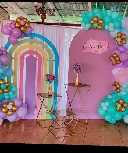 A boho-chic rainbow theme using custom arch backdrops. The decoration features pastel balloon garlands in teal and purple, with gold accents and modern geometric stands for a stylish party.