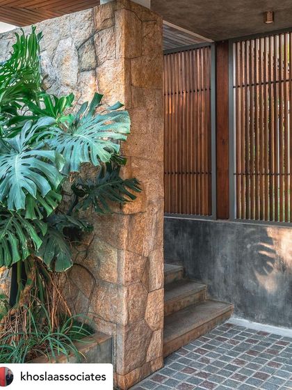 A close-up of a stone-clad pillar and wooden screen, with a large Monstera plant adding a touch of the tropics. This detail shot highlights the rich materiality and texture used to blend architecture with nature.