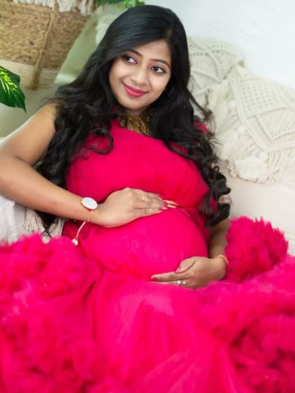 A joyful portrait in a vibrant pink ruffled gown. The mom-to-be is nestled in our cozy studio setup, surrounded by pillows and plants, radiating happiness.