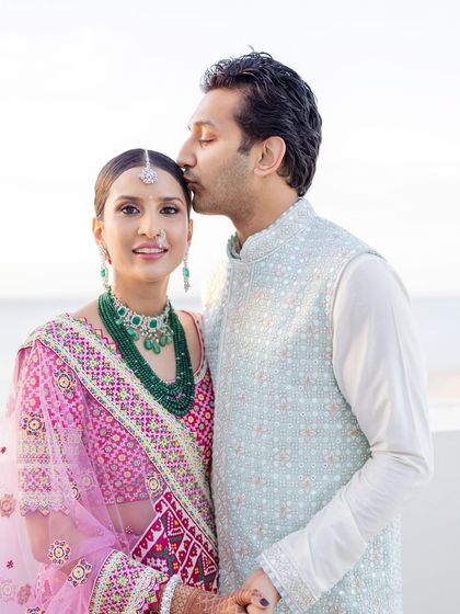 A sweet moment captured between the couple. For her, I created a clean, elegant look with a sleek bun and fresh makeup that allowed her traditional pink bandhani lehenga to take center stage.