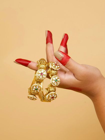 A pair of our traditional Kundan kadas, showcased by a classical dancer's hand. These bangles feature intricate work and colorful stones, perfect for festive and cultural events.