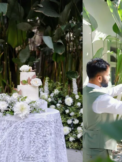 A beautiful three-tiered wedding cake adorned with fresh white roses, set on a lace-covered table. The surrounding white floral arrangements create a cohesive and elegant dessert station.