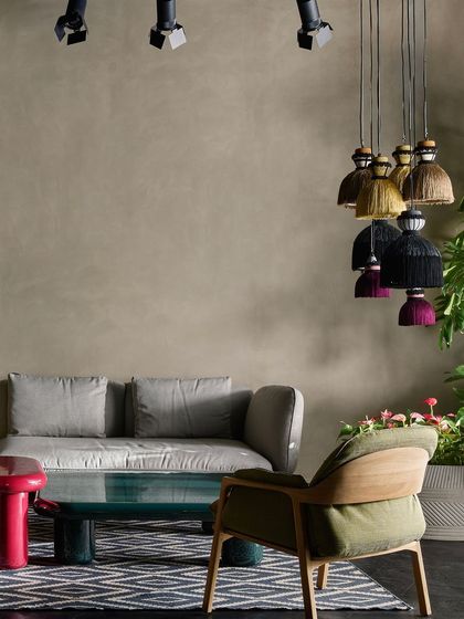 This vignette combines a simple grey sofa with a textured armchair and colorful tassel pendant lights, showing a blend of minimalist and bohemian styles.