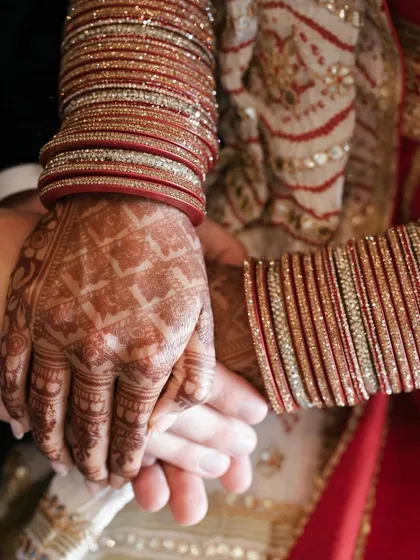 A close-up shot capturing the beautiful details of an Indo-American wedding, from the intricate henna on the bride's hands to her traditional red bangles.
