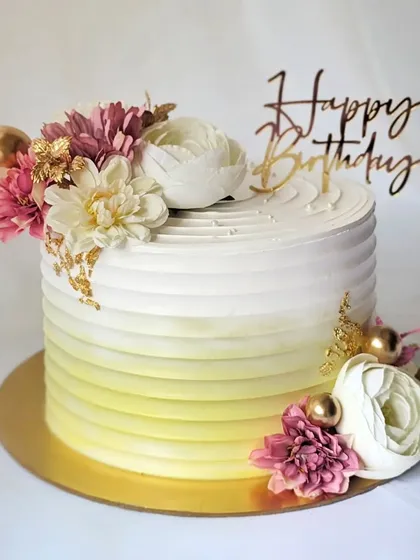 A beautiful floral cake with an ombre yellow and white finish. The design is completed with a spray of pink and white flowers.