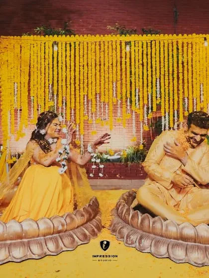 A playful moment during the haldi ceremony, with the couple seated in large lotus-shaped pots, laughing as they are covered in turmeric.