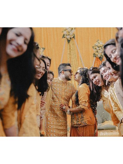 A creative shot of a couple sharing a moment, framed by their smiling friends and family during the haldi.