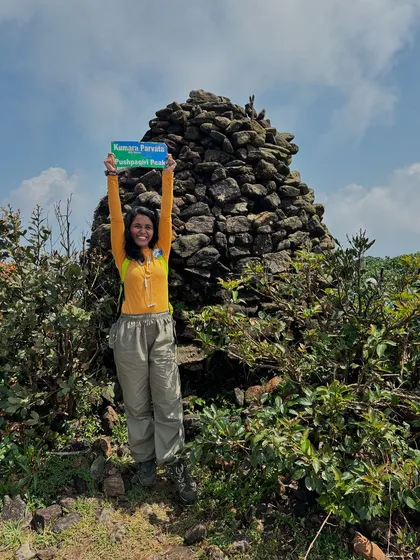 A trekker celebrating at the Kumara Parvatha summit marker.