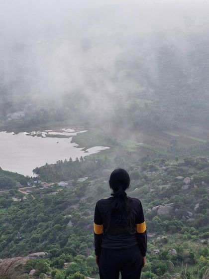A trekker looks out over the misty valley and lake from the top of Uttari Betta.