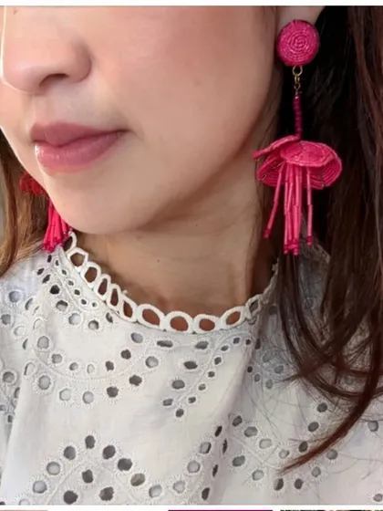 A model shot of the fuchsia floral beaded drop earrings, adding a vibrant pop of colour to a white lace top.