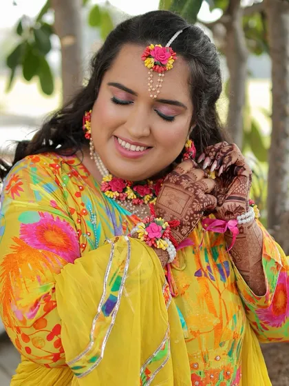 A radiant Haldi bride glowing with happiness. I created a minimal makeup look with a pop of pink on the lids and a fresh, dewy base to complement her vibrant yellow outfit and floral jewellery.